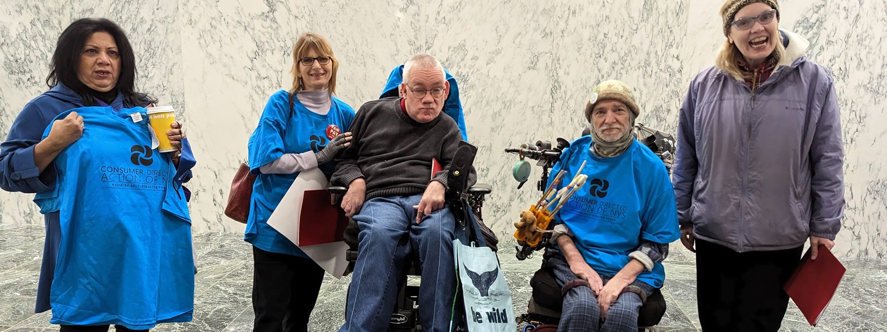 Two people in wheelchairs with three people standing.