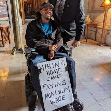 Man holding sign "hiring home care paying minimum wage"